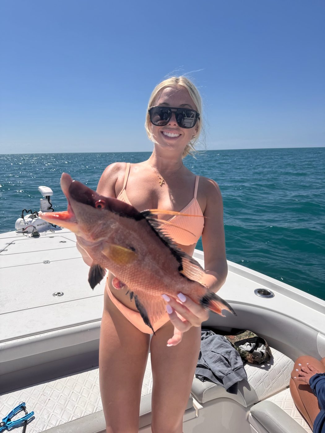 An angler on the bow holding a gag grouper up against a clear blue sky