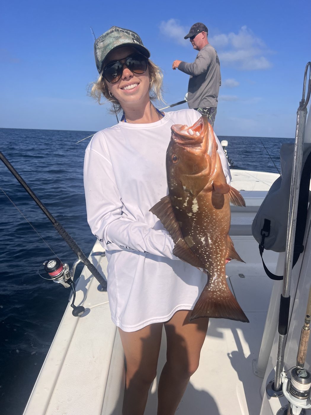 An angler holding a red grouper aboard the boat with open water behind