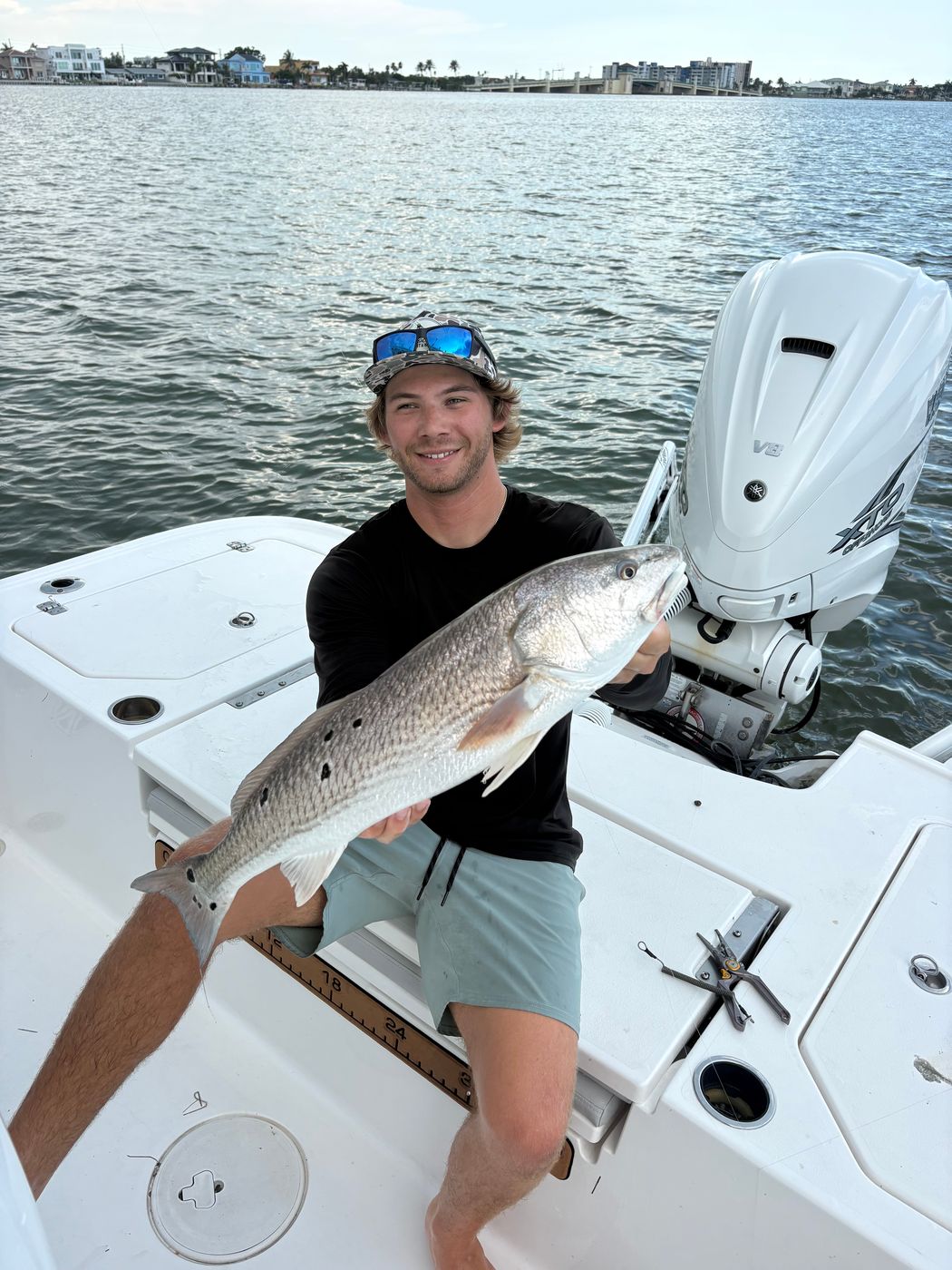 An angler seated on the deck holding a redfish, the outboard motor and open water behind