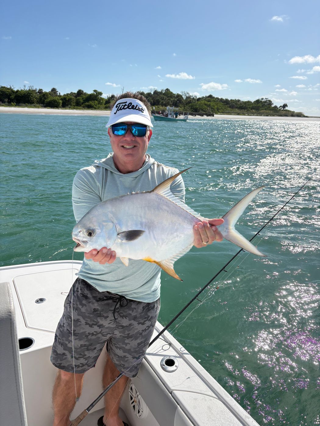 An angler on the boat holding a large silver fish with a long dark dorsal fin, sparkling water behind