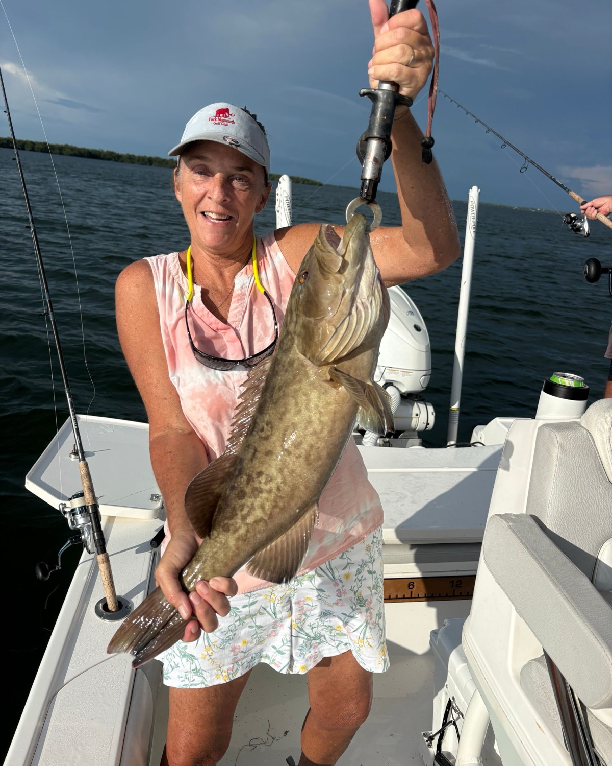 A smiling angler holding a gag grouper on a lip grip aboard the boat under a dark evening sky