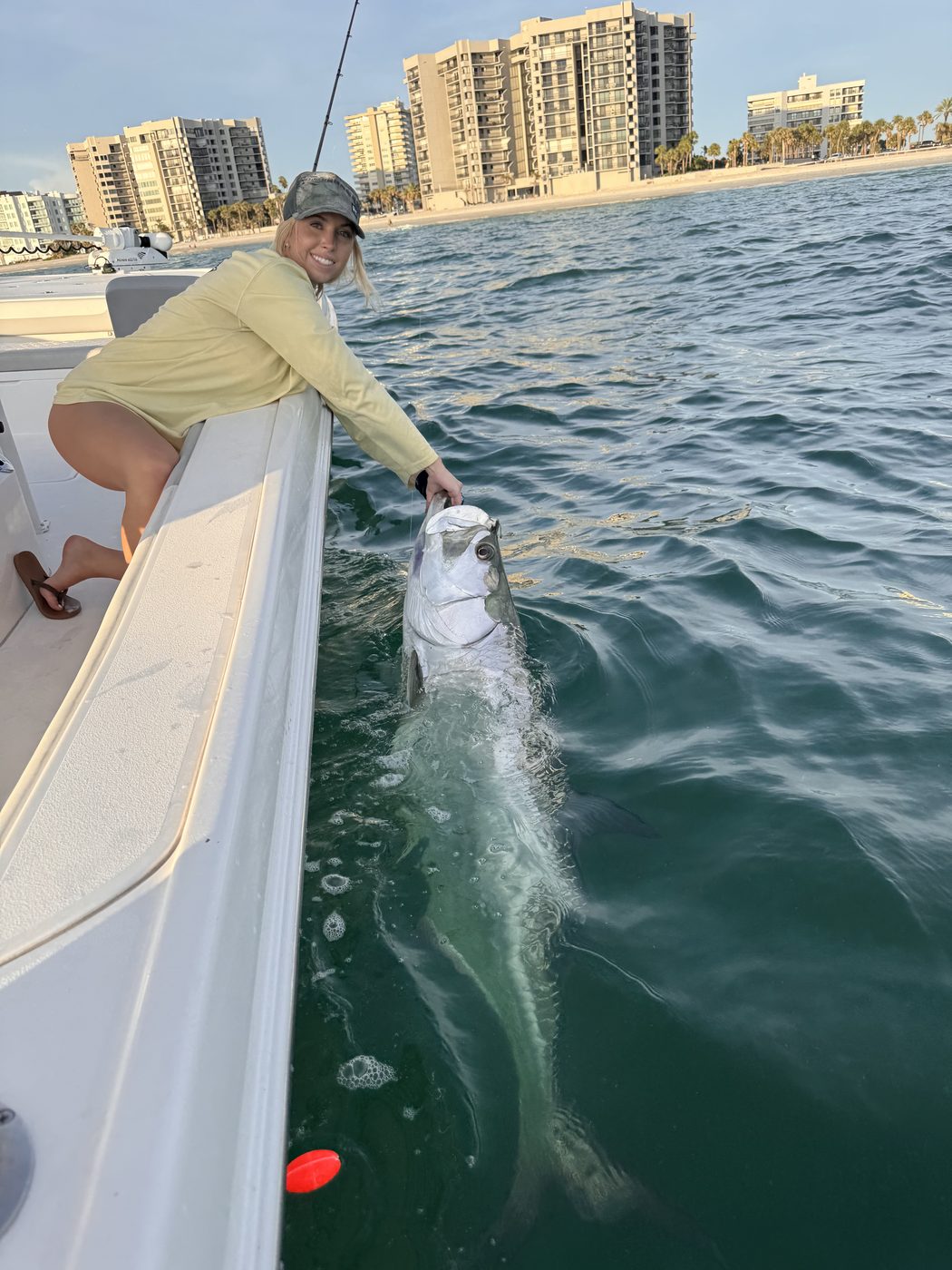 An angler kneeling on the deck holding a tarpon by the leader alongside the hull