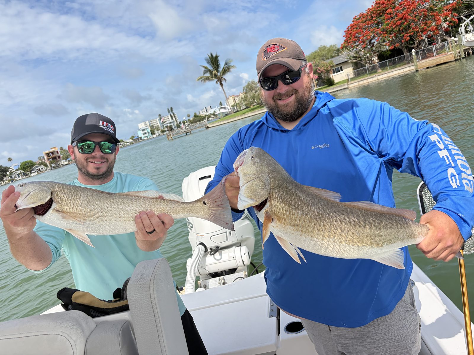 Two anglers holding up a pair of redfish with the waterfront and palms behind