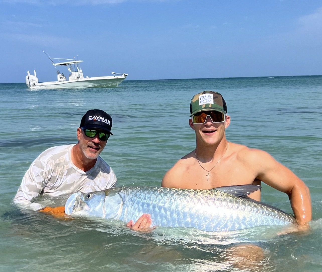 Two anglers in the shallows holding a tarpon between them for a photo