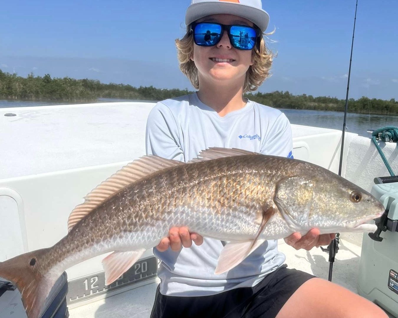 A young angler in sunglasses holding up a redfish aboard the boat